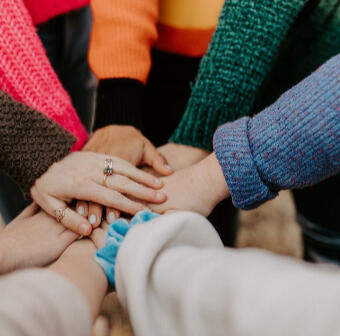 Teamwork is shown by hands laid on top of another in a circle.